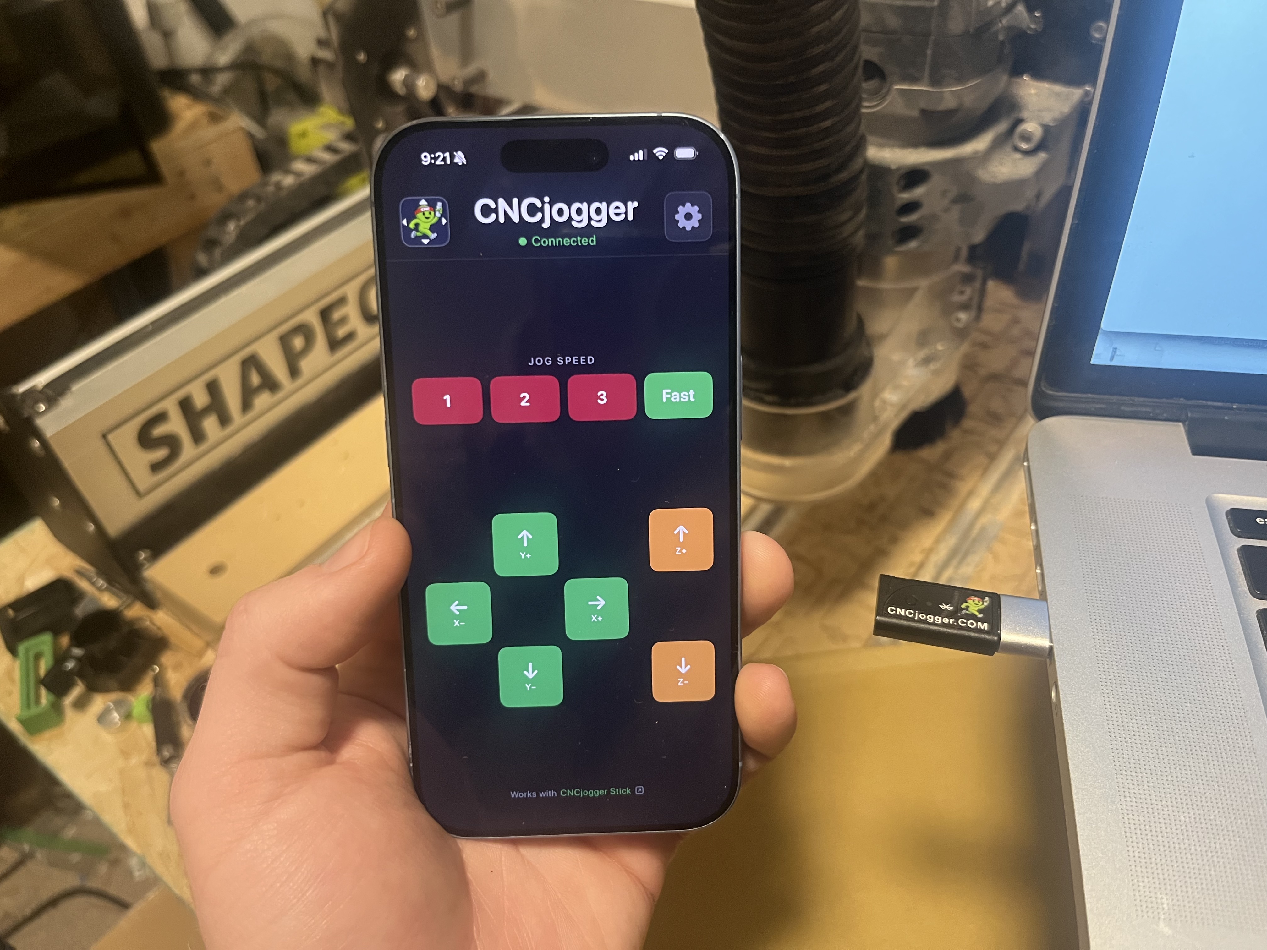 CNCjogger app on iPhone with CNCjogger Stick plugged into laptop next to Shapeoko CNC